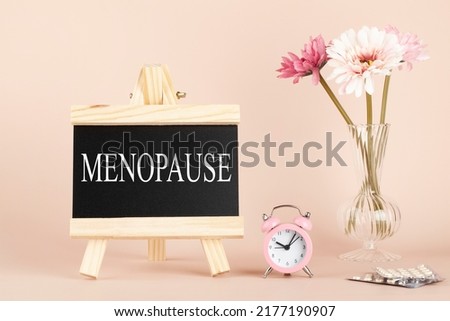 menopause word written on black board, flowers, clock and pills on beige background. women health and middle age concept. medicine, healthcare style Royalty-Free Stock Photo #2177190907