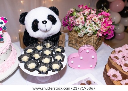 Traditional Brazilian party white brigadeiro sweets on table with plush panda bear and flowers