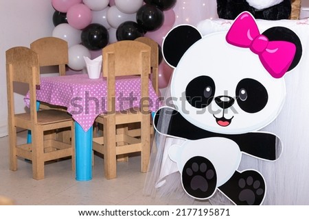 Children's table decorated with pink tablecloth with white polka dots with wooden chairs in a party hall. Panda bear cartoon with pink bow on head