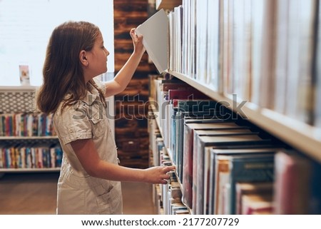 Schoolgirl choosing book in school library. Smart girl selecting books. Books on shelves in bookstore. Learning from books. School education. Benefits of everyday reading. Back to school