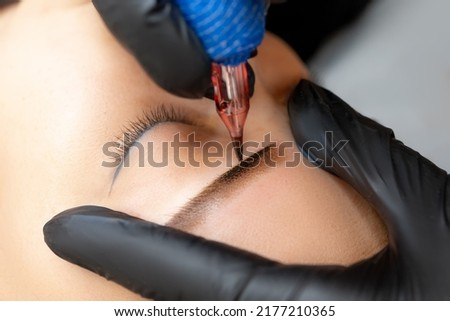 close-up master makes eyebrow tattoo apply permanent makeup on the model's eyebrows Royalty-Free Stock Photo #2177210365