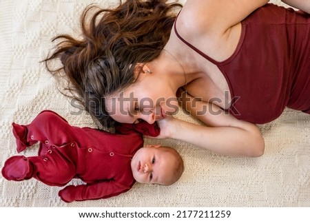 A young mother lies and looks at a newborn baby, top view