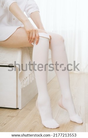 Girl putting on white stockings at home. Anti-embolic stockings. Compression Hosiery. Medical stockings, tights, socks, calves and sleeves for varicose veins and venouse therapy.