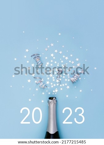 Open bottle of champagne on light blue background decorated with silver star confetti and numbers 2023. New Year celebration or party. Selective focus. Royalty-Free Stock Photo #2177215485