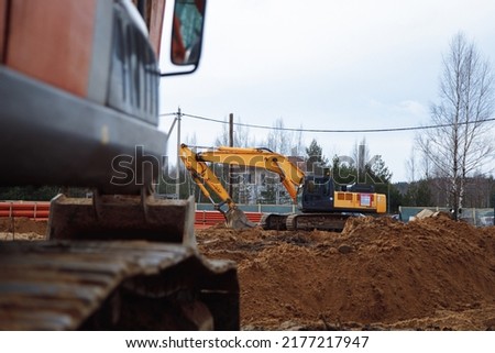An orange excavator works at a construction site and picks up sand with a bucket. High quality photo