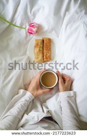 person holding cup of coffee. Breakfast in bed. coffee in bed. Pancakes for breakfast. Romantic breakfast.	