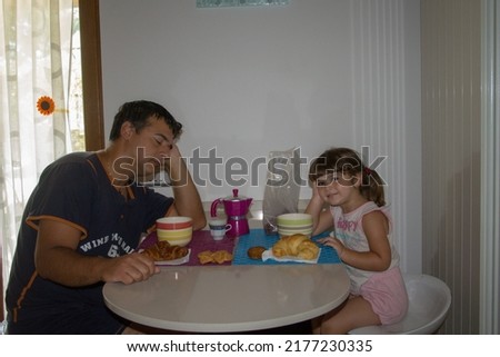 Picture of a sleepy and just waking up dad with his daughter while having breakfast in the morning.