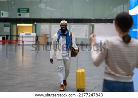 Joyful african man employee arriving in airport, moving to another country for work, relocating abroad. Happy black guy with luggage going to female waiting for him with sign board in arrivals area Royalty-Free Stock Photo #2177247843
