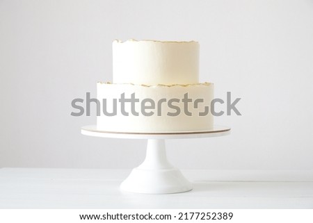 Cake with white cream, decorated with gold confectionery sprinkles on a white background. Two-tiered white wedding cake. Royalty-Free Stock Photo #2177252389