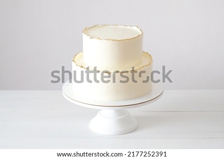 Cake with white cream, decorated with gold confectionery sprinkles on a white background. Two-tiered white wedding cake. Royalty-Free Stock Photo #2177252391