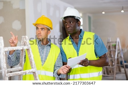 African-american man engineer and caucasian man architect talking about documents, planning repair works in apartment.
