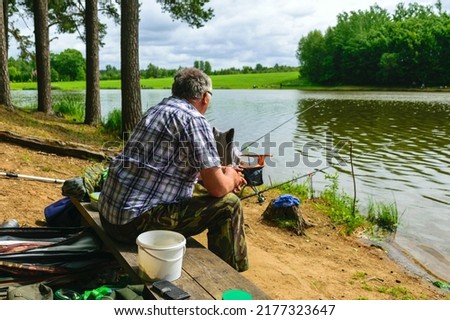 sunny photo from summer with an angler, angler sits on the shore of the lake and catches fish, Royalty-Free Stock Photo #2177323647