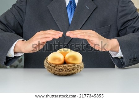 Securing investment and income protection insurance, financial concept : Investor protects a basket with golden eggs, depicting protecting long-term investment portfolio against non-commercial risk. Royalty-Free Stock Photo #2177345855