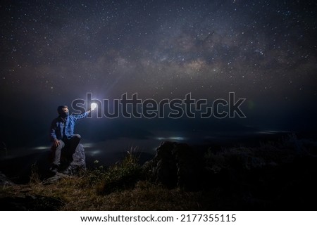 Man sit down on stone at night. Milky way galaxy at night. Milky way galaxy at night. Image contains noise and grain due to high ISO. Image also contains soft focus and blur.