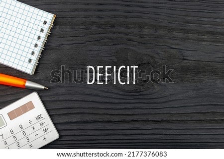 DEFICIT - word (text) on a dark wooden background, notepad. Business concept (copy space).