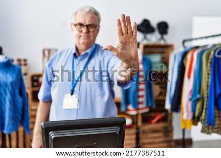 Senior man with grey hair working as manager at retail boutique doing stop sing with palm of the hand. warning expression with negative and serious gesture on the face. 