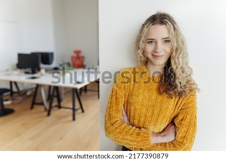 Young successful teenage girl leaning against office wall and looking into camera with smile Royalty-Free Stock Photo #2177390879