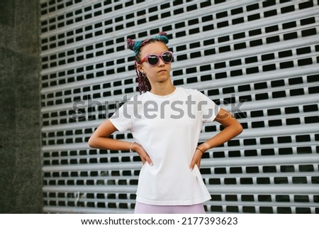 Portrait of a cute teenage girl with African braids in a white t-shirt and sunglasses stands on a city street. Mock-up for print. T-shirt template.