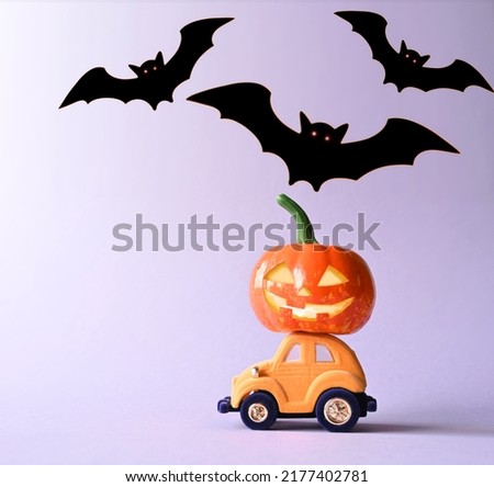 Toy car with funny pumpkin on the roof and bats on purple background. Space for text. Halloween background.
