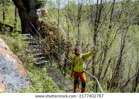 A tourist takes a selfie against the background of nature standing on an iron staircase in the mountains, a national park, a pedestrian road for tourists, a hike in the forest, a photo