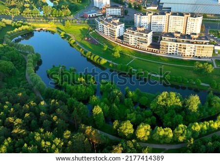 Residential high-rise buildings in the city near river. Townhouses and multi-floor home, aerial view. River in city on sunrise. Multi-storey residential building. City landscape in green background. Royalty-Free Stock Photo #2177414389
