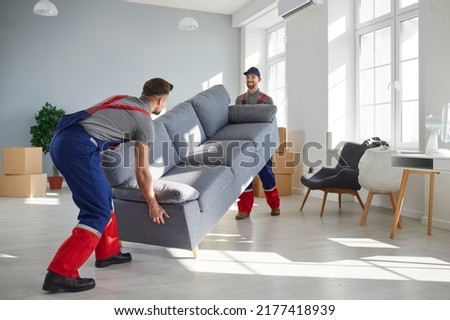 Two young workers lift up heavy sofa together. Young men from moving company and lorry delivery service removing things from the house, carrying furniture and other belongings Royalty-Free Stock Photo #2177418939