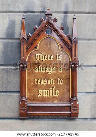 Decorative wooden sign hanging on a concrete wall - There is always a reason to smile