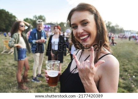 Caucasian woman showing rock music sign towards camera at music festival and friends in the background 