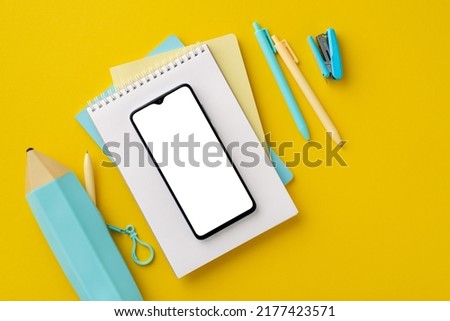 Back to school concept. Top view photo of stationery smartphone over stack of copybooks stapler pencil-case and pens on isolated yellow background with blank space