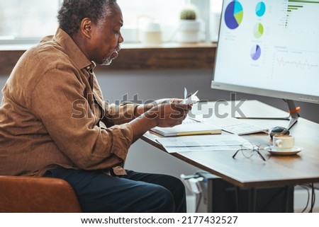 Stressed elderly grey-haired man in glasses look at laptop screen have problems paying bills taxes online. Thoughtful mature 70s male manage household finances, calculate expenses expenditures at home