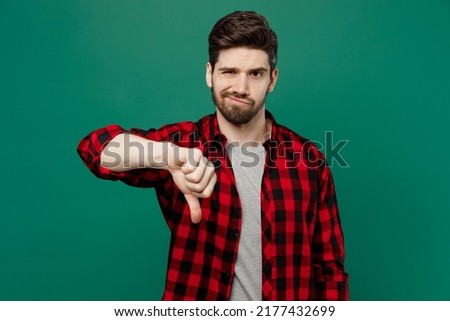 Young sad dissatisfied displeased caucasian man he 20s wear red shirt grey t-shirt showing thumb down dislike gesture isolated on plain dark green background studio portrait People lifestyle concept Royalty-Free Stock Photo #2177432699