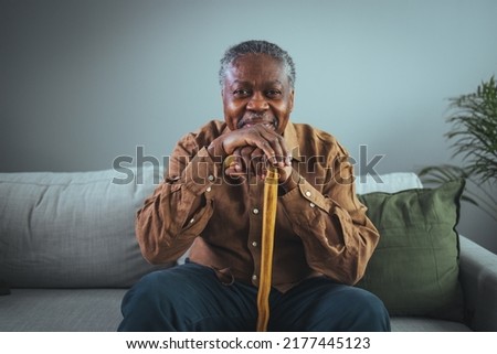 Portrait of happy senior man smiling at home while holding walking cane. Old man relaxing on sofa and looking at camera. Portrait of elderly man enjoying retirement.  Royalty-Free Stock Photo #2177445123