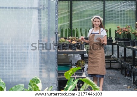 Beautiful girl using digital tablet while checking growth of potted flowers and working in a greenhouse. shop and holds cacti in her hands cactus garden