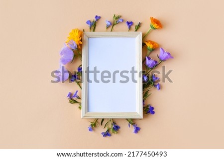 Blue bluebell, lobelia flowers and orange calendula flowers with a white text frame on an orange background. Summer flat lay