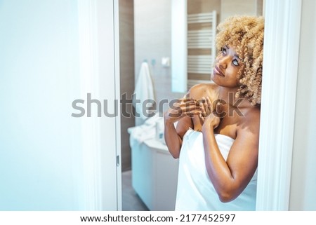 Hydrating moisturisers have saved my skin. Skin Care Concept. Beautiful african american lady wrapped in towel applying moisturizing body lotion after bath