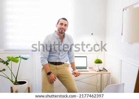 Attractive happy man leaning on his office desk while working remotely and finishing his professional work