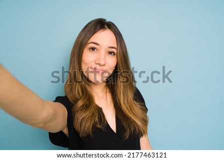 Wide angle view of a young woman stretching her arm and taking a selfie in a studio