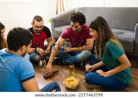 Happy group of friends playing a spin the bottle game and drinking beer together while hanging out Royalty-Free Stock Photo #2177463799