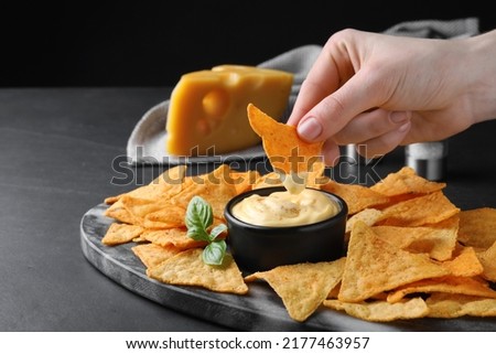 Woman dipping crispy nacho into delicious cheese sauce at black table, closeup. Space for text Royalty-Free Stock Photo #2177463957
