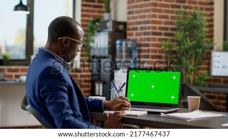 Office employee looking at laptop with greenscreen template, working in startup space. Sales consultant using isolated mockup background with chroma key display and blank copyspace.