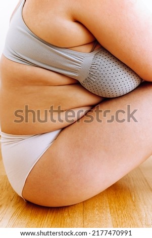 Unrecognizable curvy woman in white panties and frameless bodysuit sits on wooden parquet floor, demonstrates concept of positive body and self-acceptance. unrecognizable plus size woman Body Positive