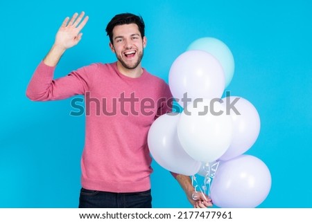 Happy Caucasian Guy Handsome Brunet Man With Bunch of Colorful Air Balloons in Pink Jumper Showing High Five Gesture Over Blue Background. Horizontal image Composition
