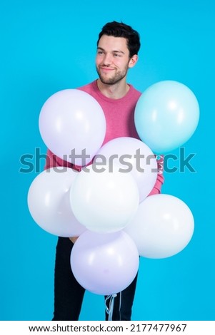 Guy Handsome Brunet Man With Bunch of Colorful Air Balloons in Pink Jumper With Positive Facial Expression Against Blue Background. Vertical Image