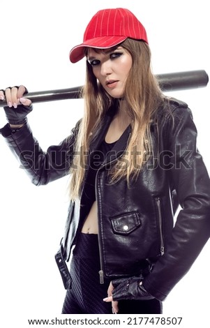 Closeup of Relaxed Winsome Caucasian Female Baseball Player Posing With Bat on Shoulder While Wearing Red Cap And Black Leather Jacket On Pure White Background. Vertical Shot