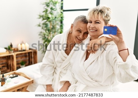 Senior caucasian couple holding credit card sitting on massage table at beauty center.