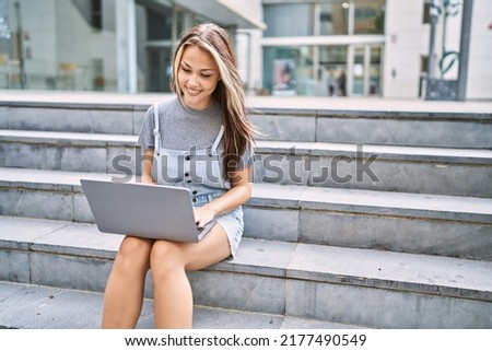 Young caucasian girl smiling happy using laptop sitting on the stairs at the city.