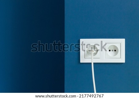 White electrical plug in the electric double socket on a blue wall Royalty-Free Stock Photo #2177492767