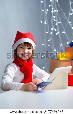 Glad Caucasian Kid Girl In Santa Hat Using Laptop for Online Gift Present Search While Using Video Calls By Webcam Chat During Holidays.Vertical Image Orintation