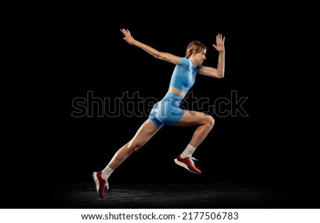 Run. Young sportive girl, long jumper in sports blue uniform performs triple jump isolated on black background. Concept of sport, action, motion, speed, healthy lifestyle. Copy space for ad Royalty-Free Stock Photo #2177506783