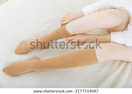 Knee socks or socks. Beige compression stockings on a woman in a white room. Girl putting on stockings at home. Beautiful female legs. Royalty-Free Stock Photo #2177514087
